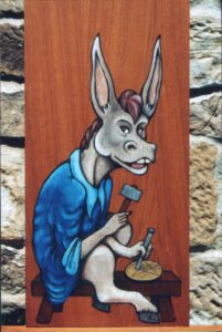 Pintura sobre madera en estilo medieval de un asno gris con camisola azul sentado sobre un banco de madera y cincelando una moneda de oro