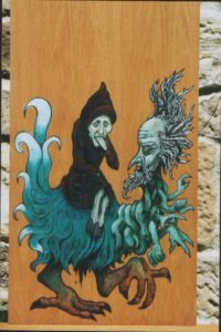 Pintura sobre madera en estilo medieval de un brujo con patas de cabra montando un monstruo con rostro barbudo y pelo desaliñado y con patas de pajarraco de cuyo intestino salen manos insidiosas