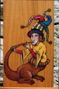 Pintura sobre madera en estilo medieval de un bufón con gorro de tricolor de tres cuerpos con cascabeles, camisa amarilla y pata y cola de león